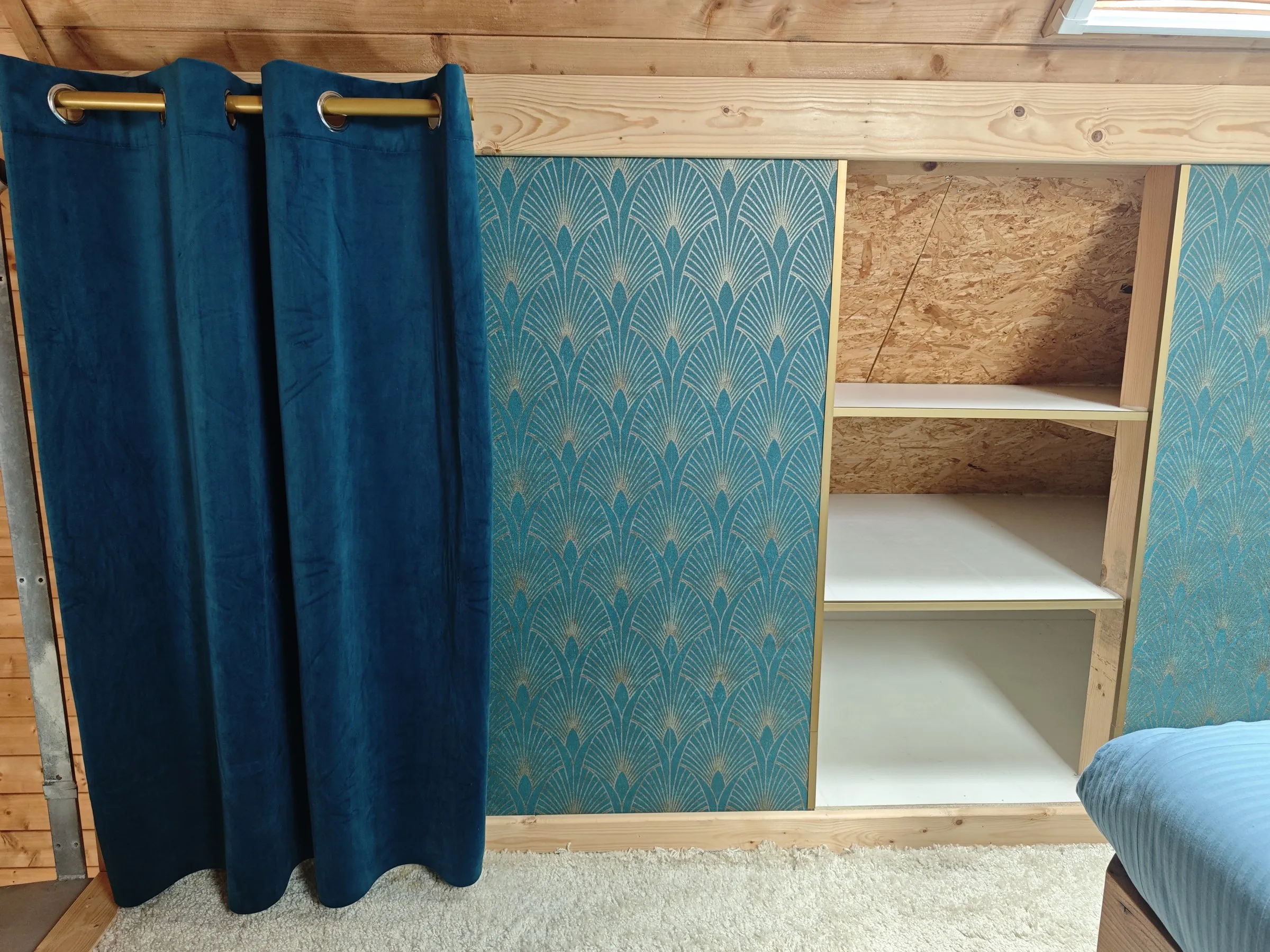 Inbouwkast met open schappen, een deur met behang en een blauw gordijn